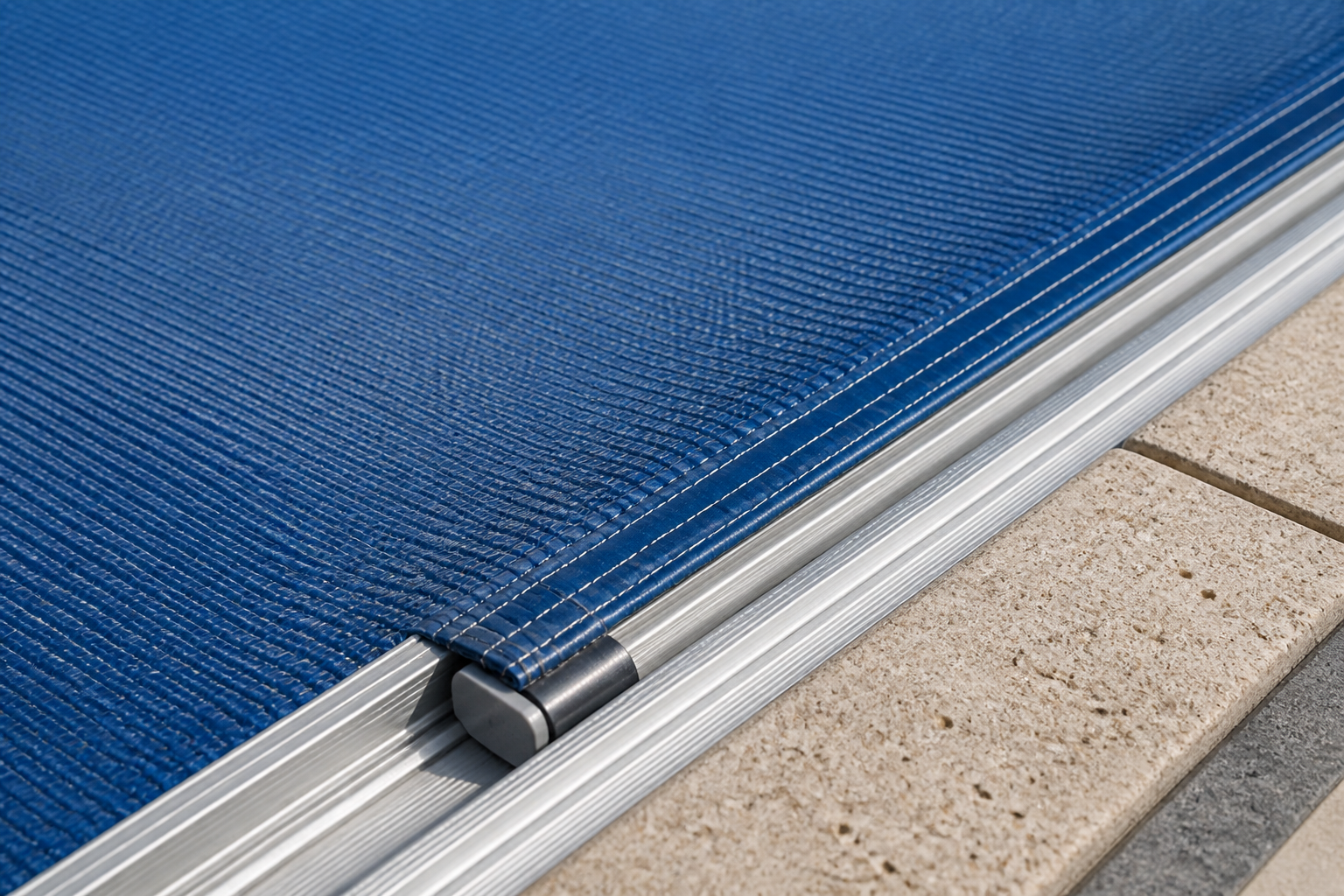 Close view of an automatic pool cover track and fabric along stone coping